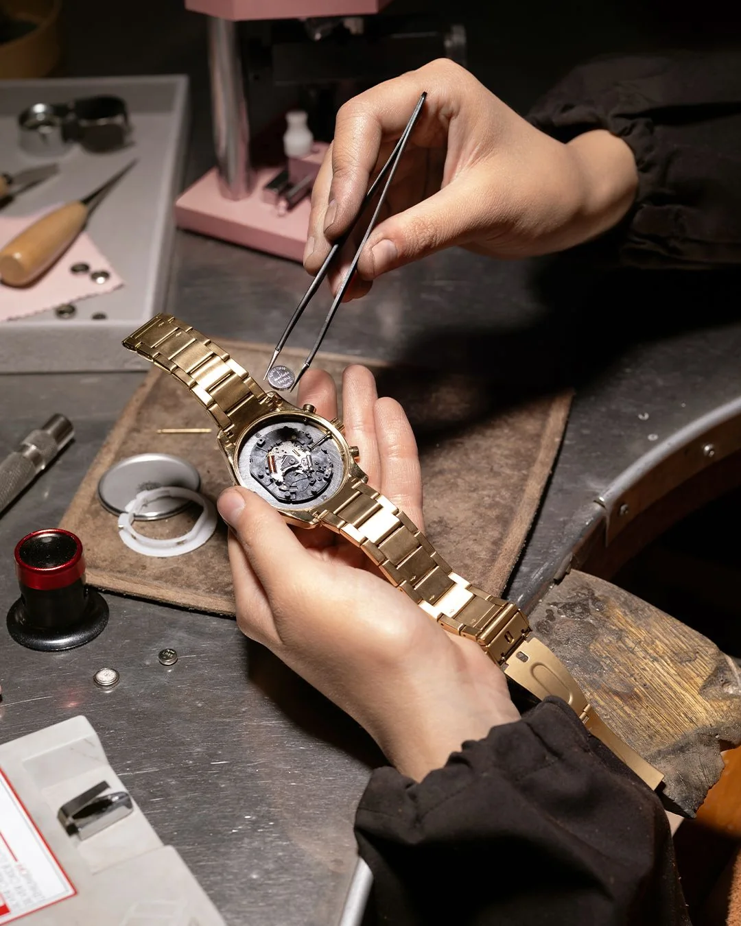 A watchmaker fitting a component to a gold bracelet watch at the bench