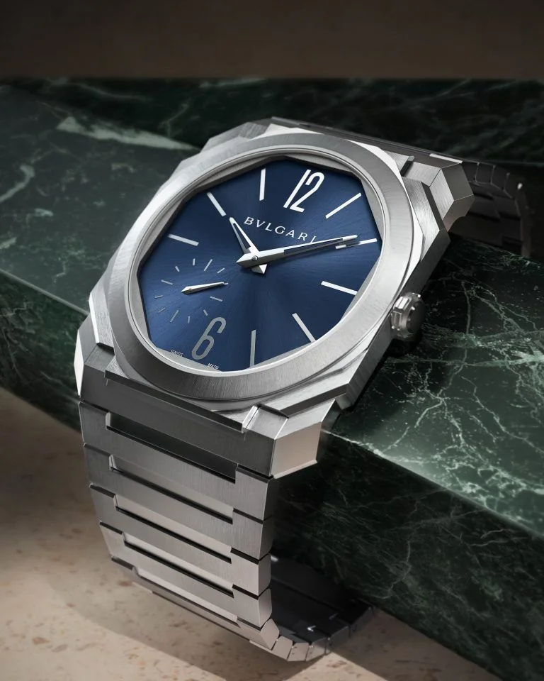 An octagonal steel watch with a blue dial resting on green marble